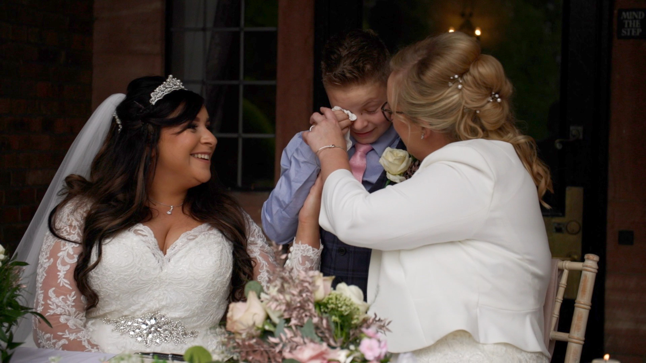 Image shows brides Sheryl and Jodie, with their son who is emotionally crying on their wedding day